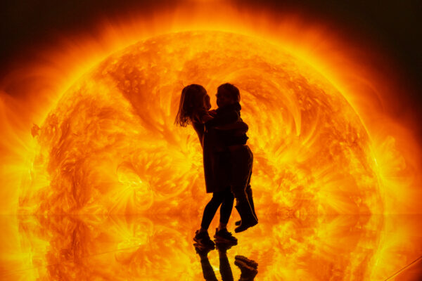 Two children infront of a bright close up image of the sun