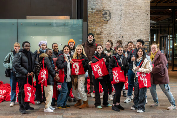 Group of young people outside all smiling holding bright red bags