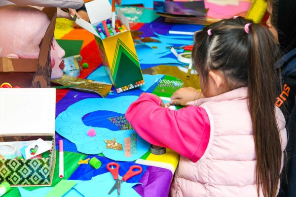 A young girl in a pink jumper and gilet enjoys craft activities.