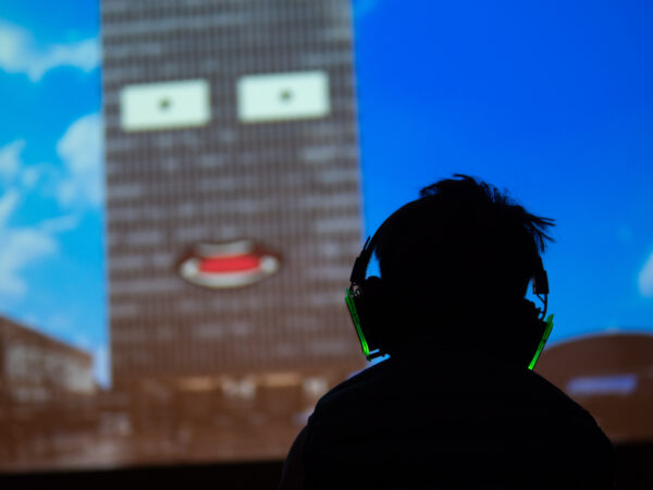 young boy with headphones on facing a projection of a building with a face